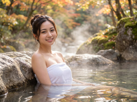 紅葉した山奥の野天風呂で白いタオルを巻き湯に浸かる女性