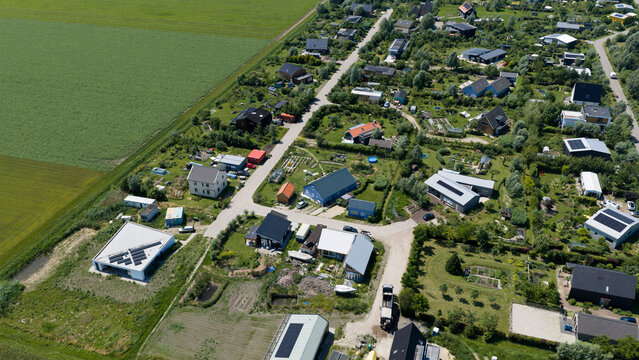 Aerial view of modern residential houses with gardens and solar panels surrounded by green fields in Almere, Flevoland, Netherlands.