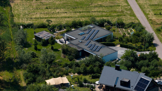 Aerial view of a modern house with solar panels on the roof, surrounded by a lush garden, trees, and a small pond in Almere, Flevoland, Netherlands.
