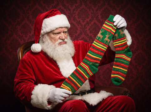 Humorous portrait of grumpy Santa Claus staring annoyed at long striped christmas socks