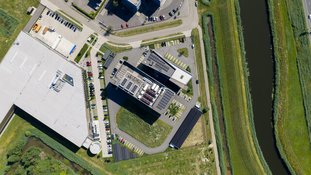 Aerial view of a modern office complex with rooftop solar panels, parking areas, and a large warehouse building near a canal in 's-Hertogenbosch, North Brabant, Netherlands.