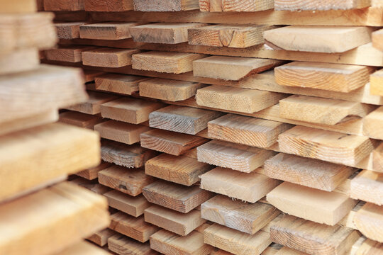 Close-up of stacked lumber boards showing detailed wood grain. Fresh sawn edges and natural texture visible. Warm light illuminates horizontal cut surface. Construction timber material supply