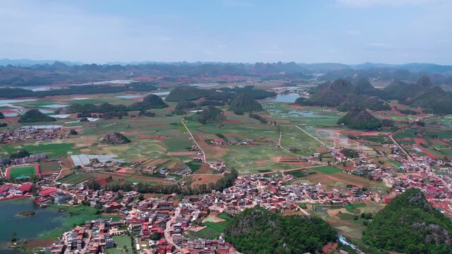 An aerial panoramic view of a rural karst region with scattered villages, farmlands, and water bodies under a clear sky.