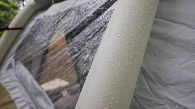 Raindrops rest on the textured white surface of an inflatable camping tent beam. Moisture beads on the waterproof fabric during a storm, highlighting the durable material and functional design