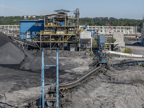 Aerial view of an industrial coke plant with conveyor belts, large piles of coal, and processing machinery under a clear blue sky in Poland.