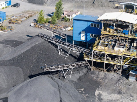 Aerial view of a coking plant with large piles of coal, industrial conveyor belts, and blue metal structures in Poland.
