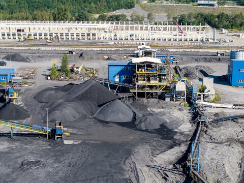 Aerial view of a coking plant with large piles of coal, industrial machinery, conveyor belts, and construction site in Poland.