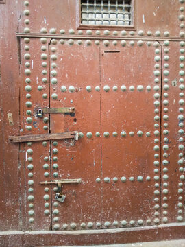Weathered brown antique wooden door decorated with numerous metal studs and secured by rusted iron padlocks shows historical craftsmanship found in traditional old city architecture