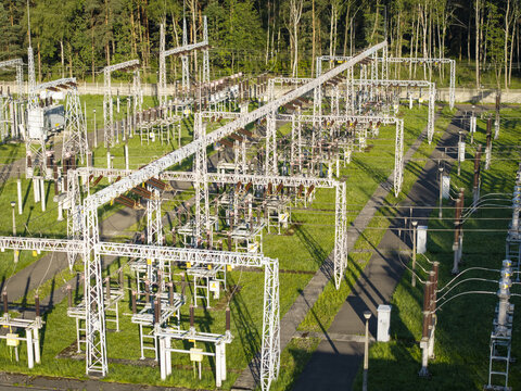Aerial view of a high-voltage electrical transformer station with metal structures, power lines, and green grass in Poland.