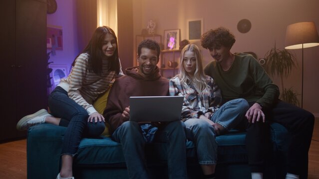 Group of friends are gathered and sitting on sofa. Youth are communicating and gesturing. Young people are looking at laptop and laughing, Friends spending spare time together and having fun.