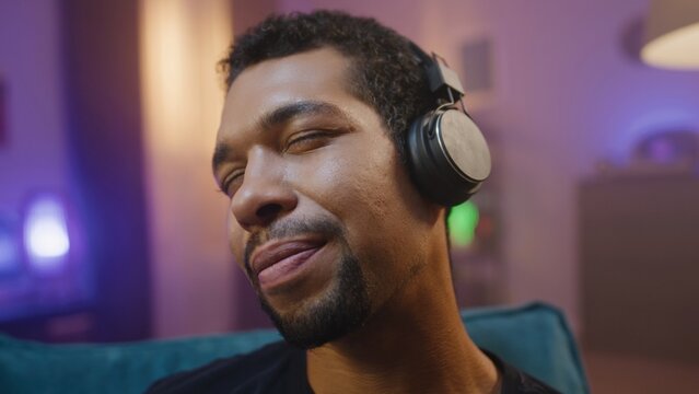 Close-up portrait of african american at unfocused background. Young man is wearing headphones and listening to music. Guy with head in hands enjoying sound. Ethnic diversity.