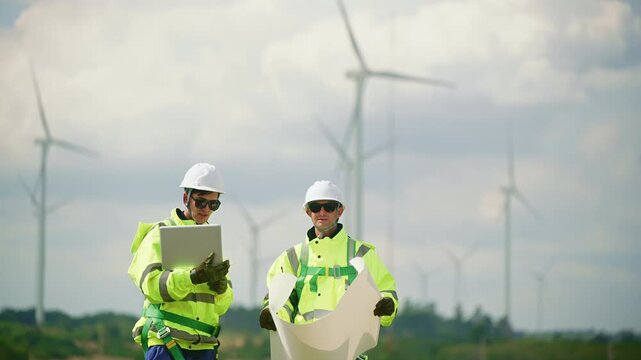 Engineers wearing safety helmets and jackets inspecting a wind turbine at wind farm at sunset. Concept renewable energy, sustainable technology wind power maintenance and environmental engineering.