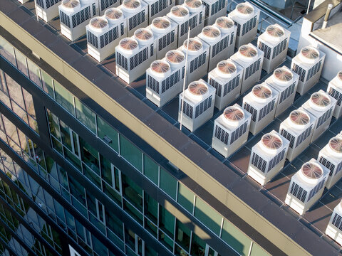 Aerial view of numerous HVAC cooling units installed on the flat roof of a modern building, likely an AI data center, with glass facade and metal framing in POLAND.