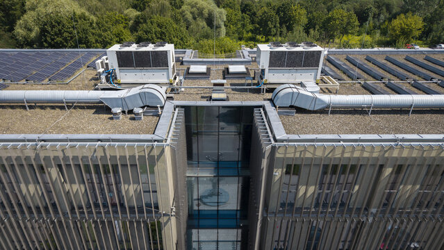Aerial view of an AI data center roof featuring large HVAC cooling units, rows of solar panels, and a central glass atrium surrounded by trees in Poland.