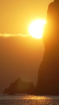 Sunset ocean cliff dramatic golden sunset over the sea with a large rock formation silhouette against a vibrant orange sky