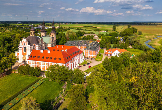 Aerial view of Cistercian Abbey in Lad with its distinctive red roofs, twin towers, and surrounding lush green landscape, fields, and a winding river in Lad, Greater Poland Voivod, Poland.
