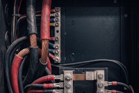 A detailed close-up shot of thick, exposed stranded copper wires and heavy-duty electrical cables connected inside a dark industrial power distribution panel.
