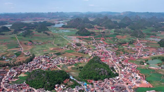 A high-angle aerial panorama shows a rural settlement nestled among karst mountains and farmlands.