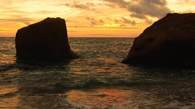 Rocks, ocean, sunset, dramatic sea stacks framing horizon waves during golden hour.