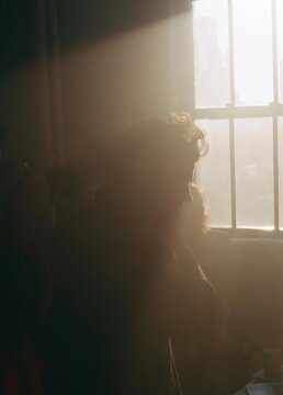 Silhouette of a person standing in front of a window. the person is facing away from the camera, with their head turned towards the right side of the image.