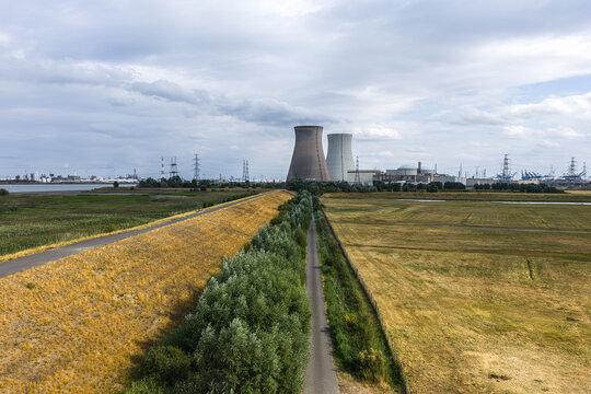 Aerial view of the Doel Nuclear Power Plant with its cooling towers rising above surrounding fields, meadows, and a narrow path under a cloudy sky in Beveren, Vlaanderen, Belgium.