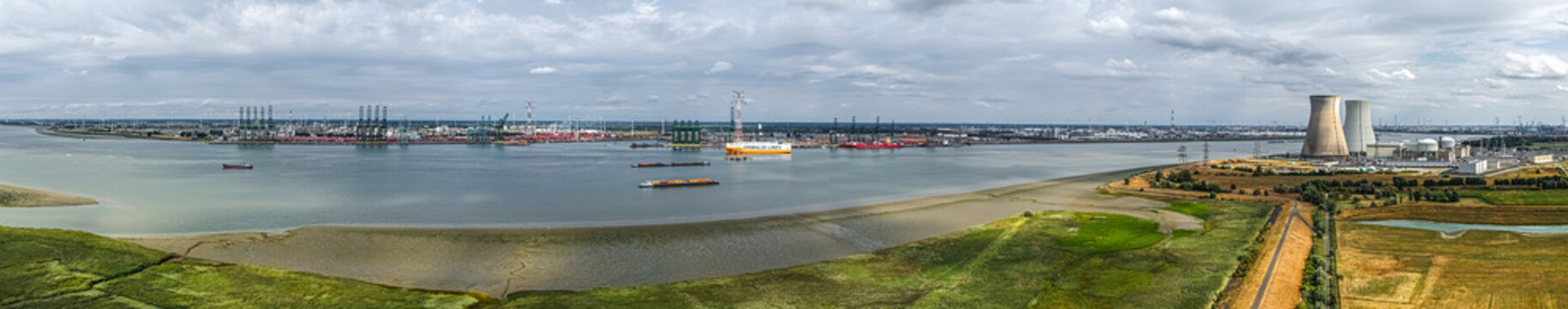 Aerial view of the Doel Nuclear Power Plant along the Scheldt river with industrial port facilities and cargo ships under a cloudy sky in Beveren-Kruibeke-Zwijndrecht, Vlaanderen, Belgium.
