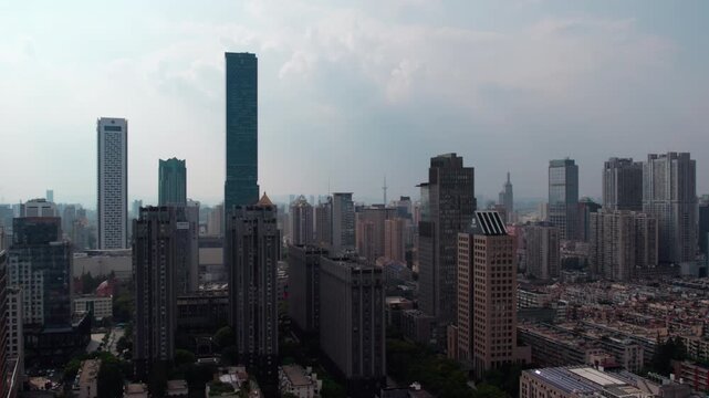 A wide aerial view of a dense modern urban skyline featuring multiple tall skyscrapers under hazy overcast skies.