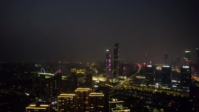 A panoramic night view of a modern urban area featuring illuminated skyscrapers and lit roads.