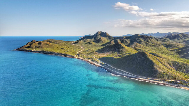 Aerial view of the coastline and mountains of Parque Nacional Cabo Pulmo with turquoise waters and a winding road in Cabo Pulmo, Baja California Sur, Mexico.