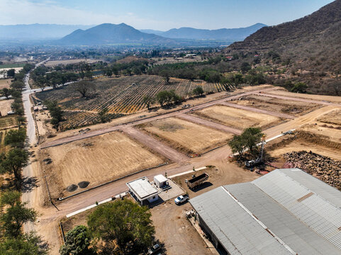 Aerial view of the El Pedregal residential division under construction with cleared land plots, dirt roads, and an industrial building in Tuxpan, Jalisco, Mexico.