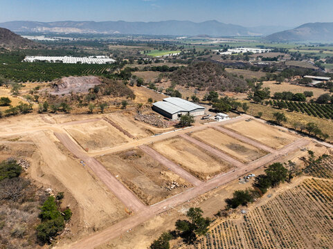 Aerial view of El Pedregal residential division under construction with dirt roads and cleared plots surrounded by agricultural fields and mountains in Tuxpan, Jalisco, Mexico.