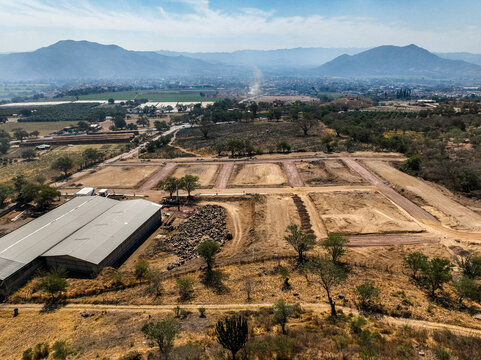 Aerial view of El Pedregal residential division in Tuxpan featuring cleared land plots, dirt roads, a large warehouse, and surrounding mountains in Tuxpan, Jalisco, Mexico.