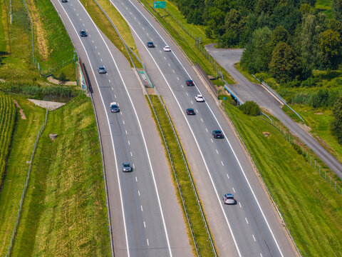 Aerial view of Droga Ekspresowa S7 with cars traveling along the multi-lane highway surrounded by green embankments and trees in Paslek, Warmian-Masurian Voiv, Poland.