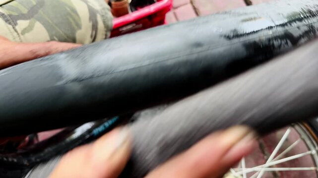 A close-up of a person's hand holding a heavily damaged bicycle tire with a large tear or hole in the sidewall. Showing a flat tire needing repair or replacement on a concrete ground.