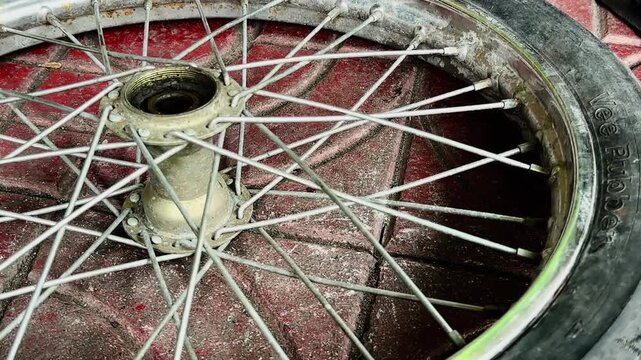 A close-up of a person's hand holding a heavily damaged bicycle tire with a large tear or hole in the sidewall. Showing a flat tire needing repair or replacement on a concrete ground.
