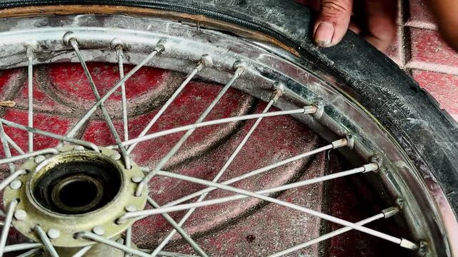 A close-up of a person's hand holding a heavily damaged bicycle tire with a large tear or hole in the sidewall. Showing a flat tire needing repair or replacement on a concrete ground.