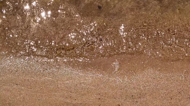 Close view of wet beach sand with a shallow wash of seawater forming layered textures along the shoreline, travel advertising, beach tourism, environmental media, coastal texture, seaside calm