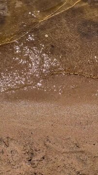 Wet beach sand meets a shallow shoreline with a thin layer of seawater and textured grains, creating a natural coastal detail, travel advertising, beach tourism, environmental media, coastal texture