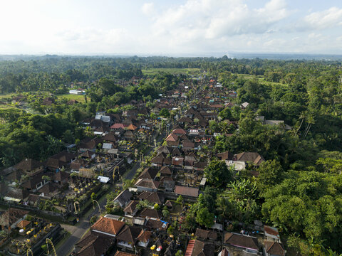 Aerial view of a traditional Balinese village featuring ornate rooftops, lush greenery, and ceremonial penjor bamboo poles lining the streets in Kecamatan Tegallalang, Bali, Indonesia.