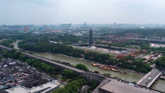 Aerial perspective of a riverside city featuring a pagoda, green spaces, roads and boats.