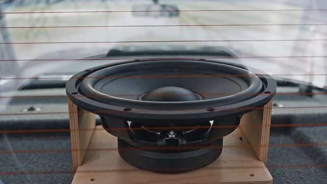 Close-up Shot of Car Audio Subwoofer Speaker Driver Mounted in Wooden Enclosure Through Rear Window