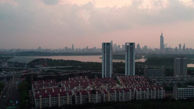 A wide shot of a modern urban area featuring twin high-rise towers, a lake, distant skyline, and residential buildings at dusk.