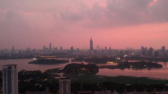 A panoramic view of a city skyline across a lake during dusk, with pink-hued sky and urban silhouettes.