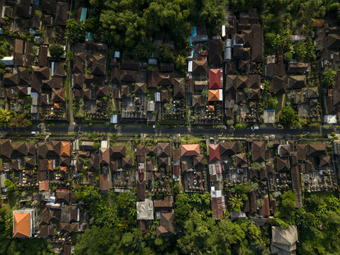Aerial view of a traditional Balinese village featuring dense rooftops, lush tropical greenery, and decorative penjor bamboo poles lining the road in Kecamatan Tegallalang, Bali, Indonesia.