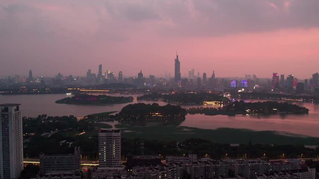 A panoramic urban landscape featuring a lake and tree-covered islands, with a city skyline visible during soft dusk twilight.