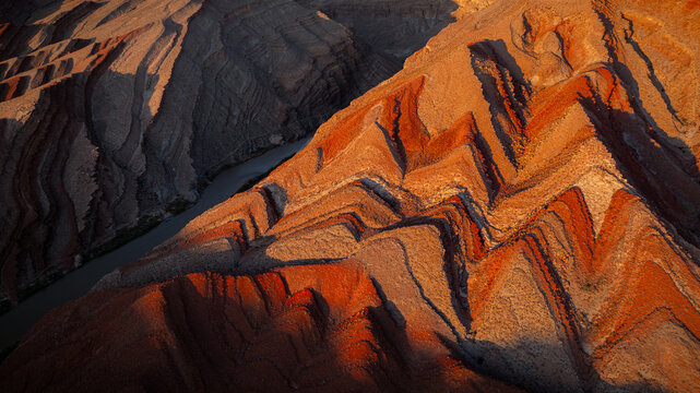 Aerial view of the dramatic geological rock formations and folded strata along the Colorado River, illuminated by golden hour light in Moab, Utah, United States.