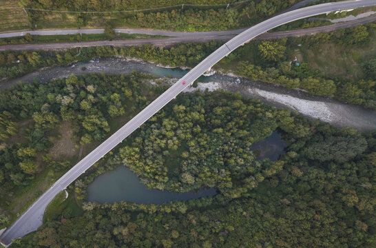 Aerial view of a bridge spanning a river surrounded by lush green forest and a small pond in Gassano, Tuscany, Italy.