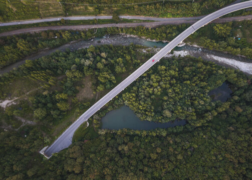Aerial view of a bridge spanning a river surrounded by dense forest and lush greenery in Gassano, Tuscany, Italy.