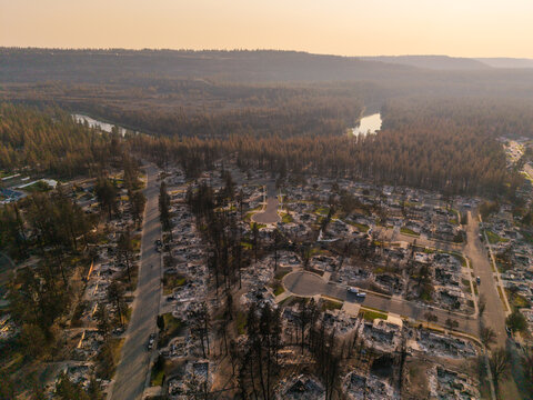 Aerial view of devastated residential area showing extensive wildfire damage with charred trees and burnt house foundations near a river in Spokane, Washington, United States.