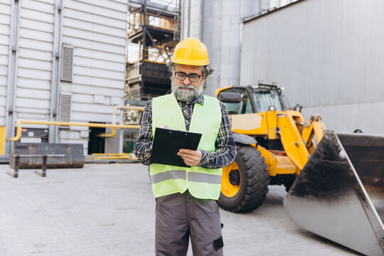 Senior male worker or inspector checking inventory and safety regulations at a modern granary elevator facility